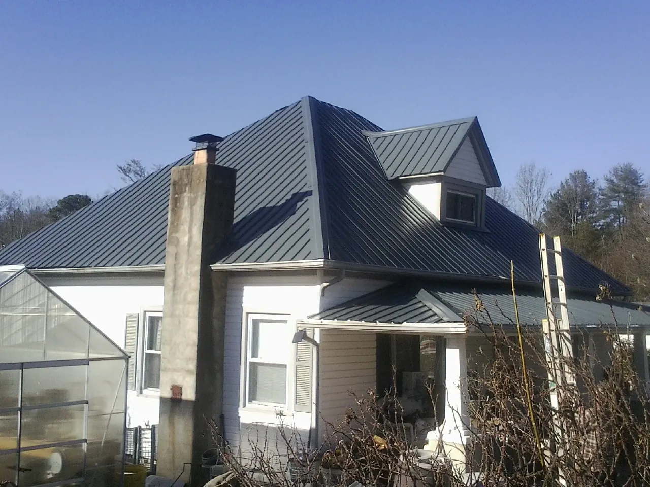 Dark blue standing seam metal roof on a white farmhouse with dormer — Slate & Tile Roof Repair by Roofing Brothers in Mount Horeb