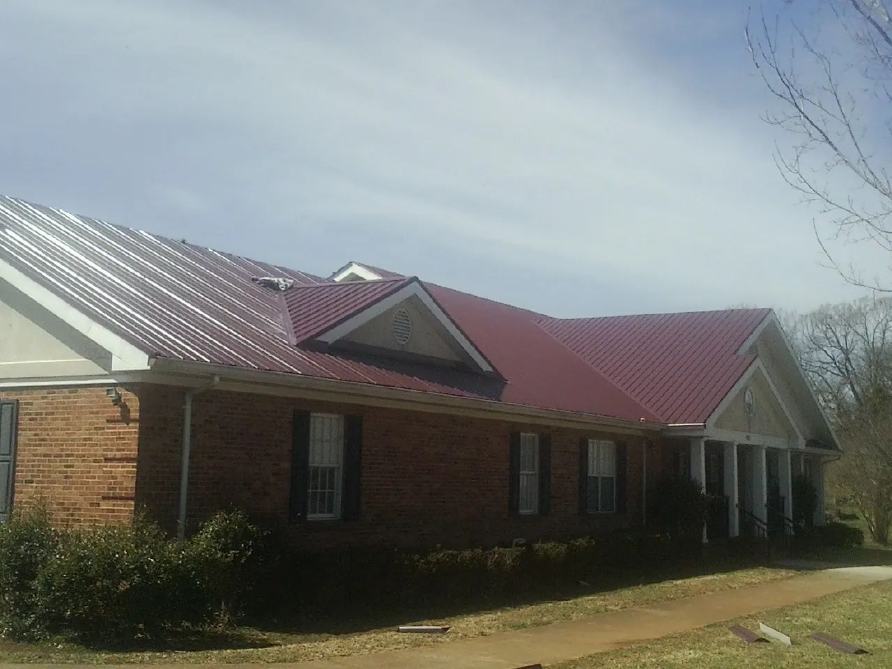 Red metal roof with gabled entries on a long brick building, from a Hail Damage Roof Repair job in Mount Horeb