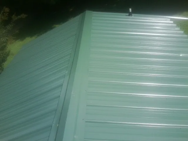 New green metal panels meeting at the ridge of a roof — Flat Roof Repair work by our crew in Mount Horeb