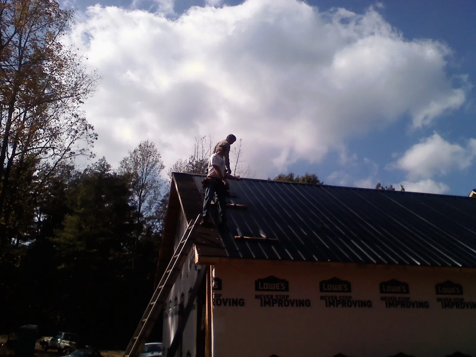 Roofer fastening dark metal panels high against a cloudy sky, from a Roof Inspection job in Mount Horeb