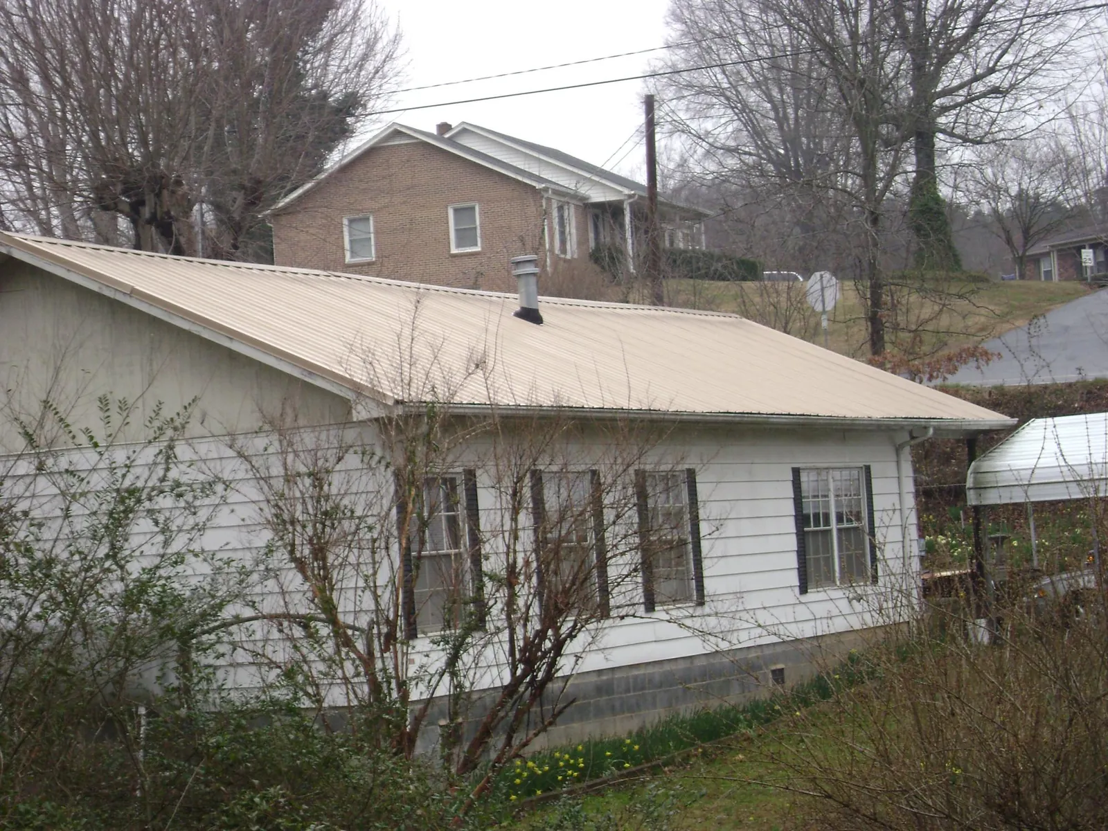 Tan metal roof on a white sided house set into a hillside — Commercial Roofing by Roofing Brothers in Mount Horeb